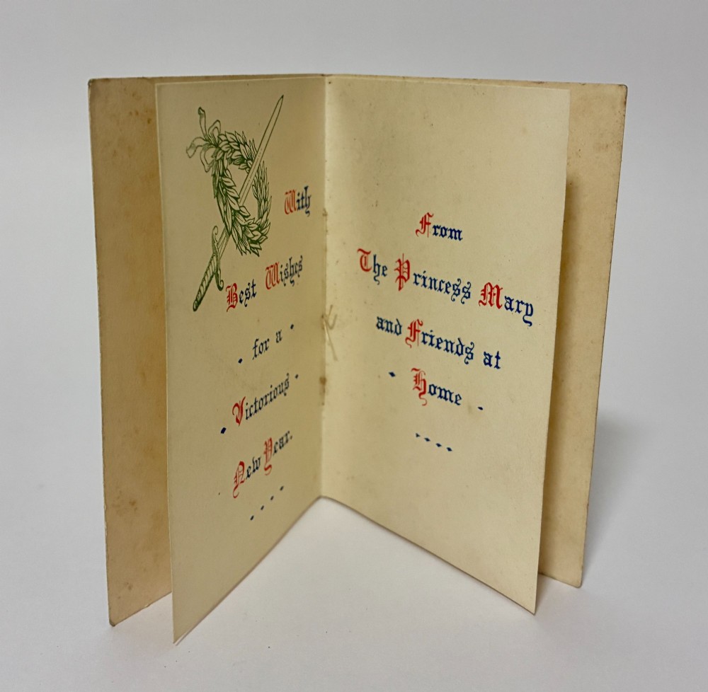 An embossed rectangular brass Princess Mary Christmas tin alongside its original cream greeting card printed with a red royal monogram. View XII