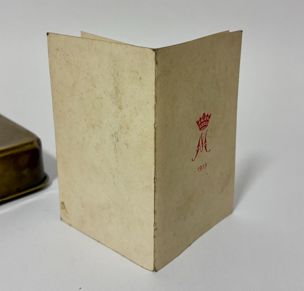 An embossed rectangular brass Princess Mary Christmas tin alongside its original cream greeting card printed with a red royal monogram. View XIII