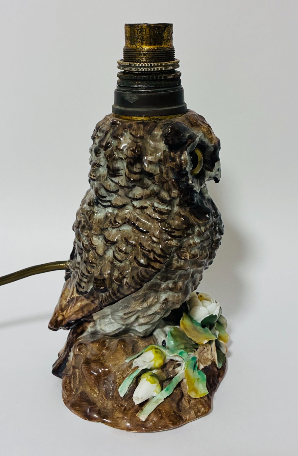 A glazed ceramic table lamp base crafted in the shape of an owl with yellow glass eyes, standing on a foliage-adorned base beneath a brass bulb holder. View IV