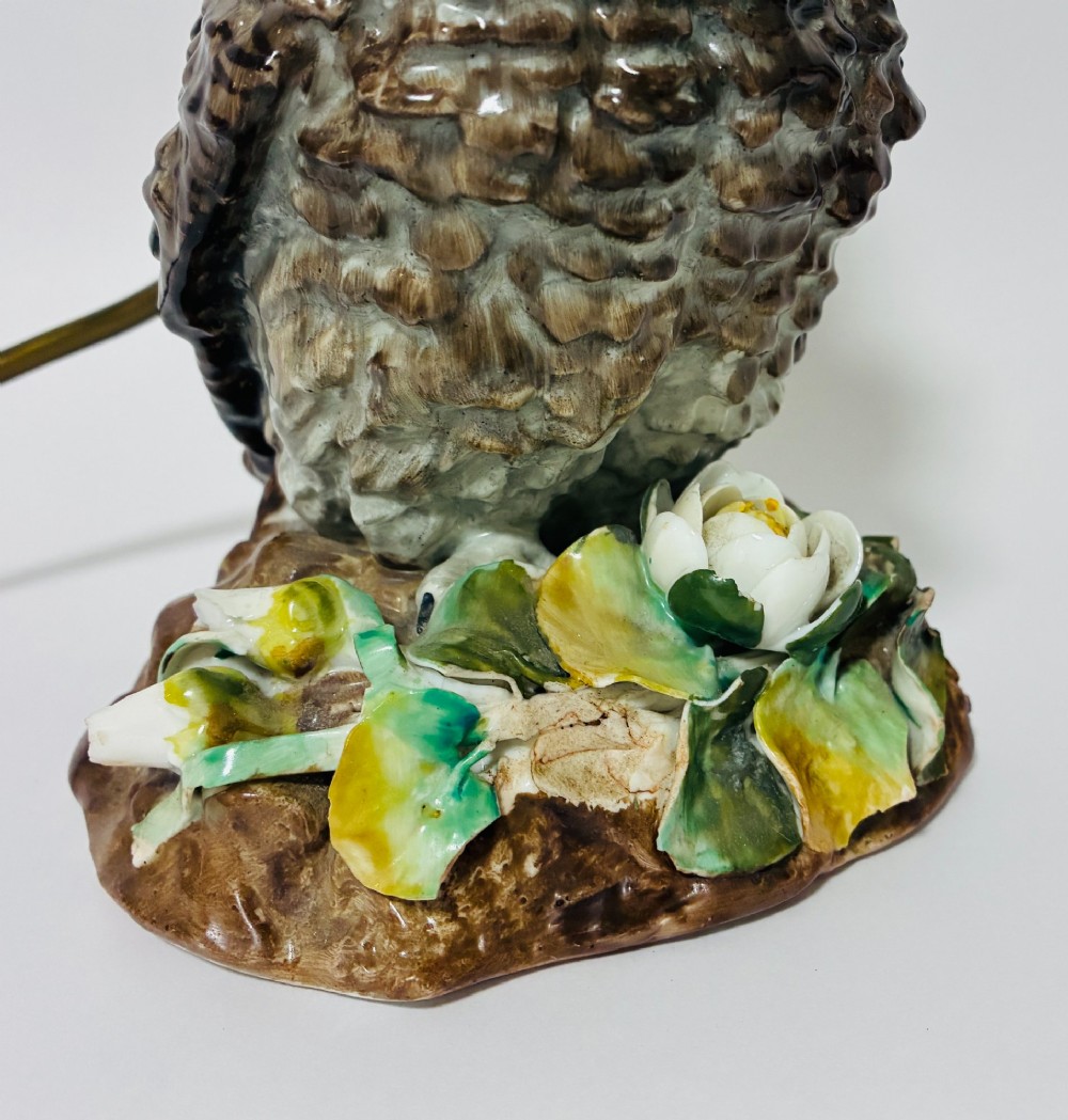 A glazed ceramic table lamp base crafted in the shape of an owl with yellow glass eyes, standing on a foliage-adorned base beneath a brass bulb holder. View V