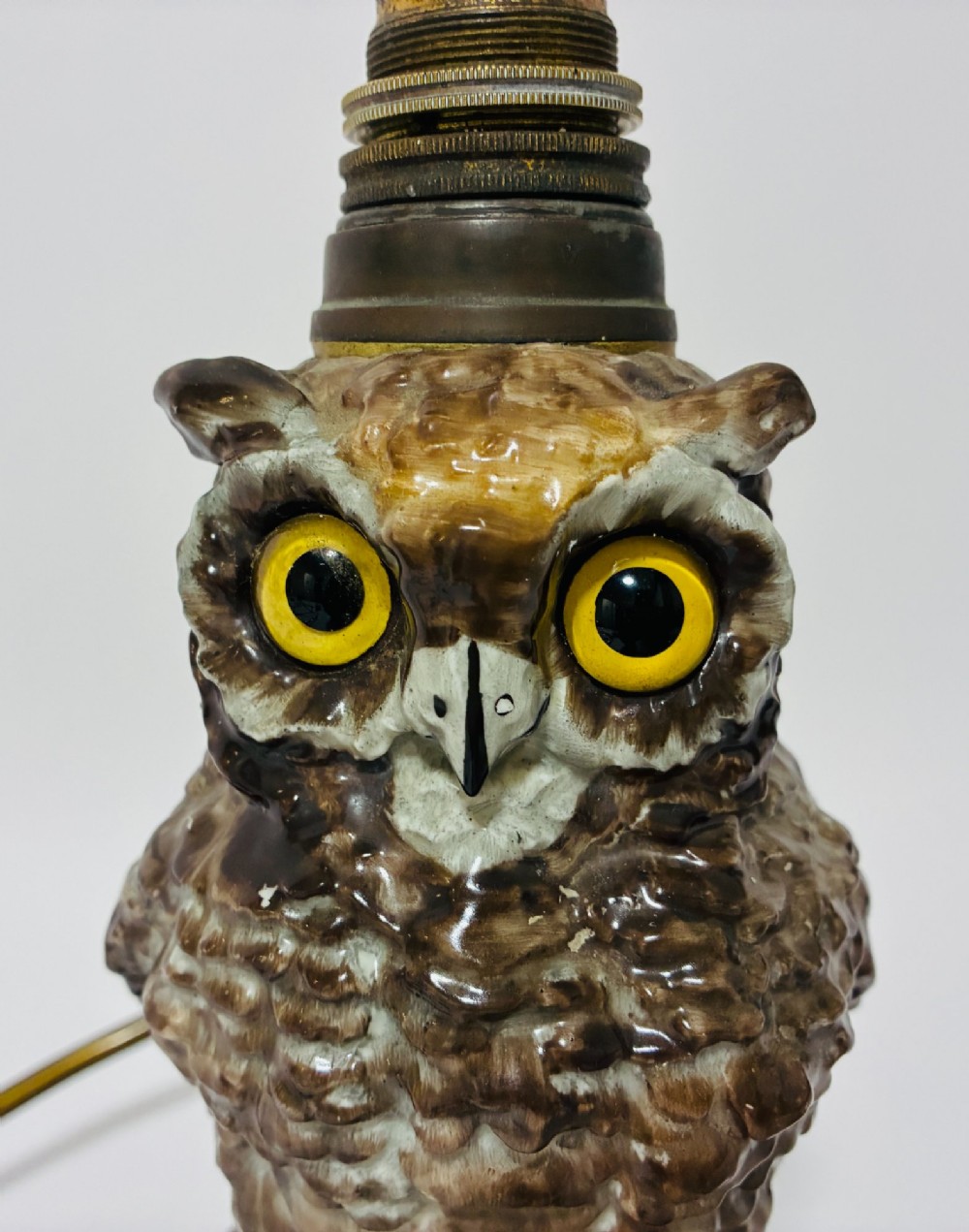 A glazed ceramic table lamp base crafted in the shape of an owl with yellow glass eyes, standing on a foliage-adorned base beneath a brass bulb holder. View VII