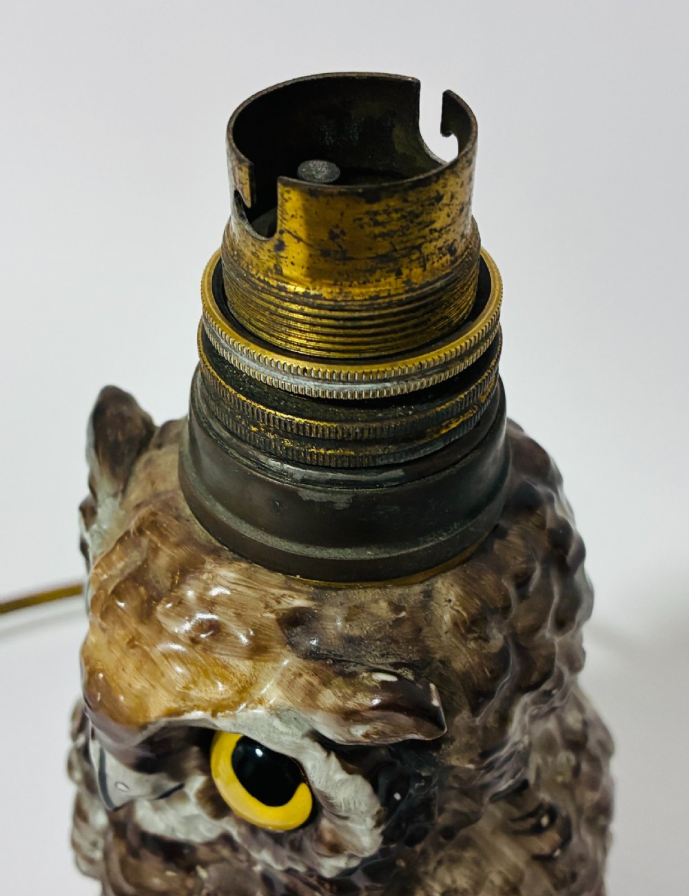 A glazed ceramic table lamp base crafted in the shape of an owl with yellow glass eyes, standing on a foliage-adorned base beneath a brass bulb holder. View VIII