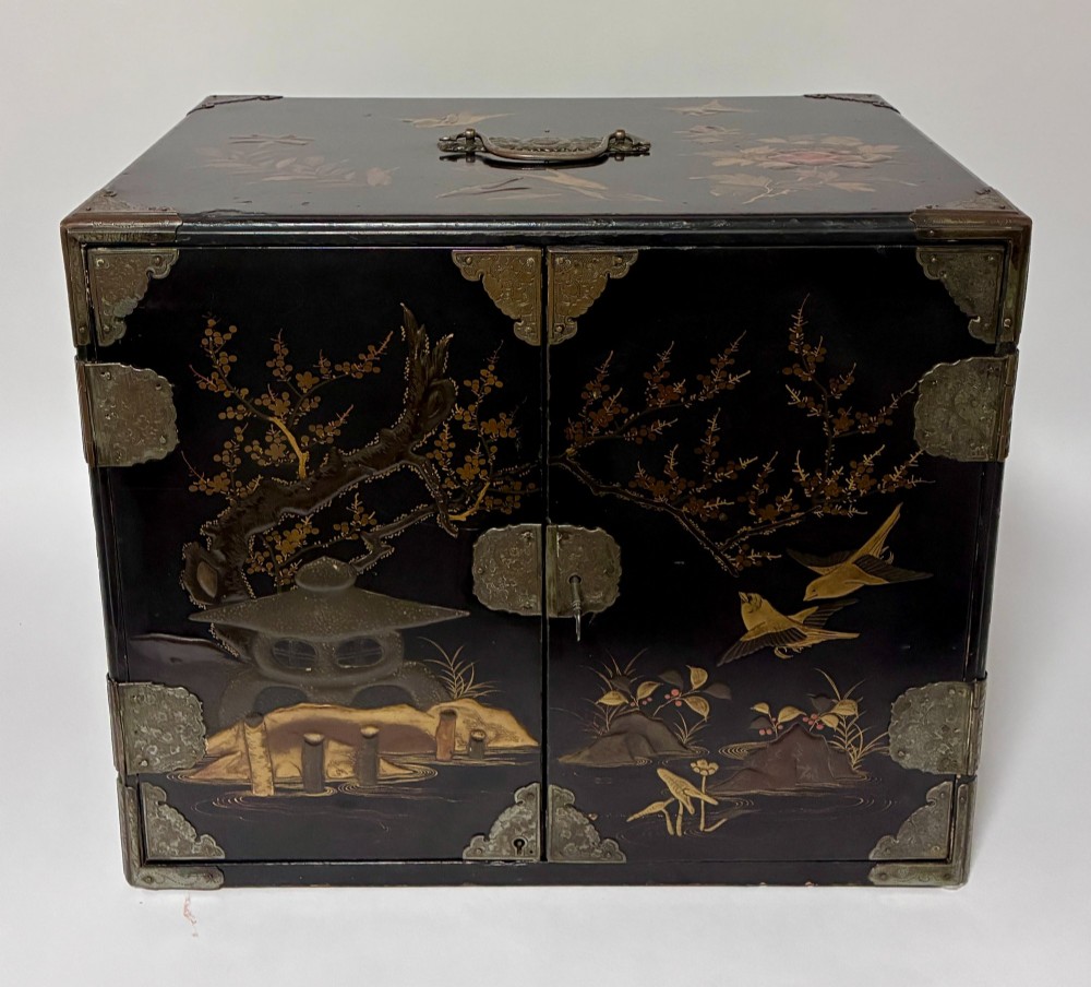 An antique Japanese black lacquer table cabinet decorated with gold bird and landscape scenes, fitted with metal corner brackets and a top handle.