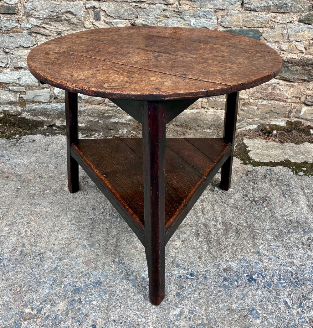 An antique Georgian dark oak cricket table featuring a circular planked top resting on three straight legs with a lower triangular shelf.