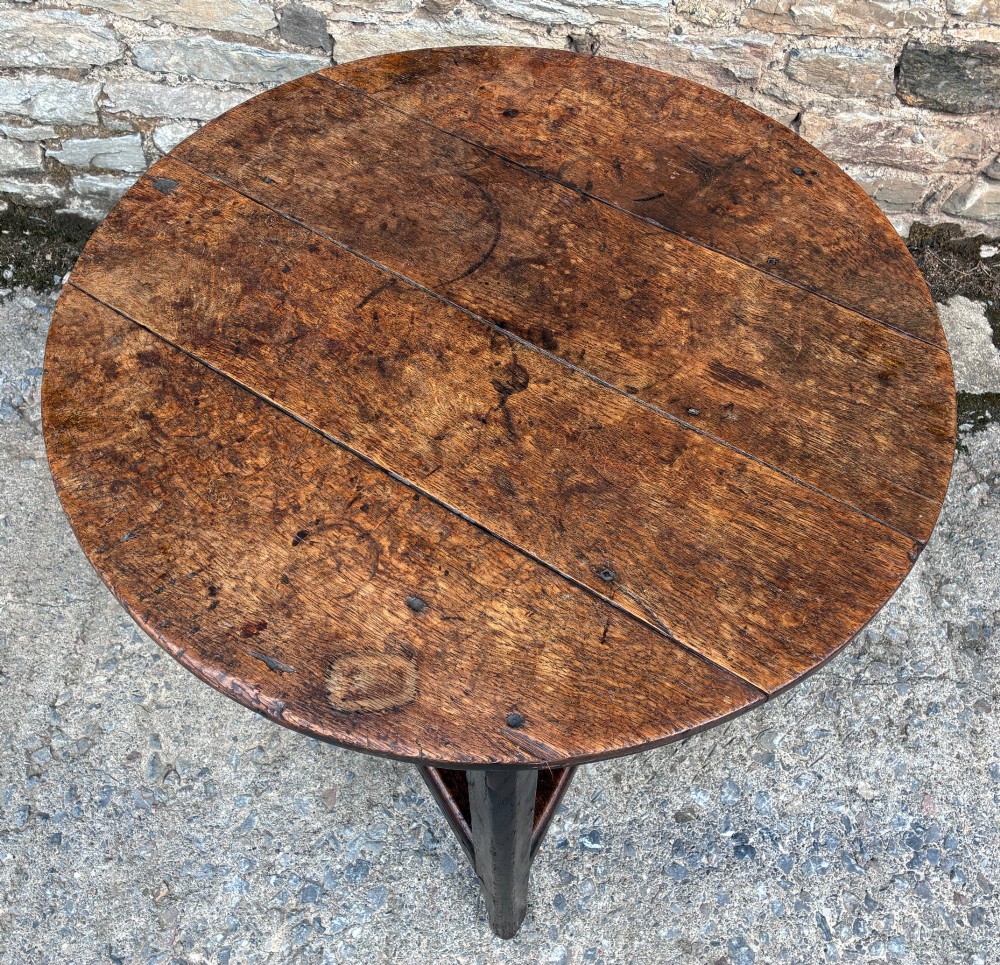 An antique Georgian dark oak cricket table featuring a circular planked top resting on three straight legs with a lower triangular shelf. View II