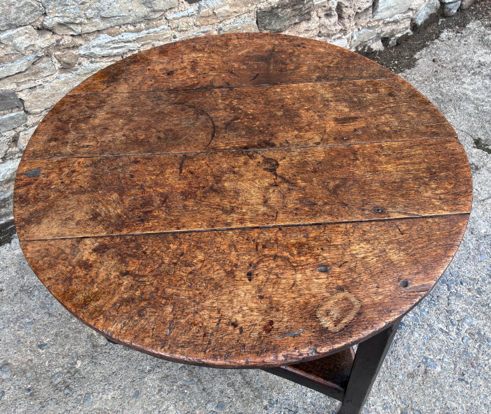 An antique Georgian dark oak cricket table featuring a circular planked top resting on three straight legs with a lower triangular shelf. View III