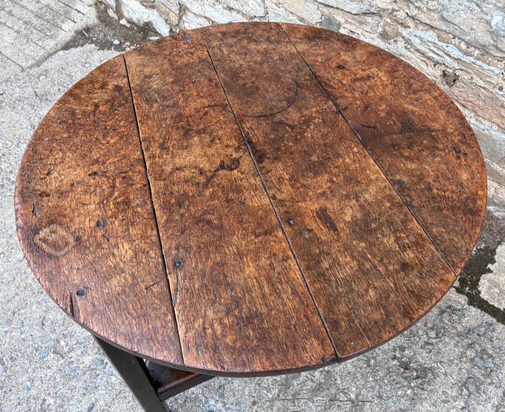 An antique Georgian dark oak cricket table featuring a circular planked top resting on three straight legs with a lower triangular shelf. View IV