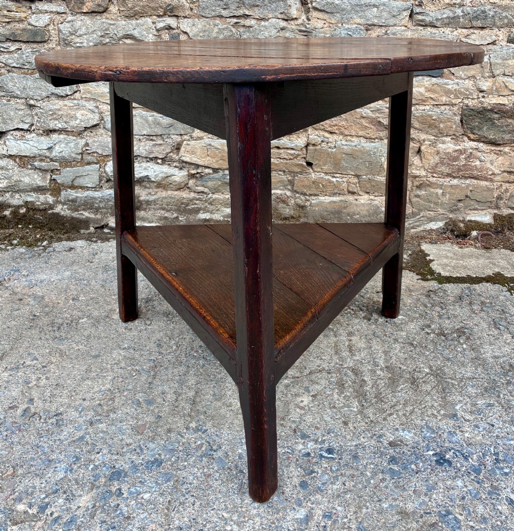 An antique Georgian dark oak cricket table featuring a circular planked top resting on three straight legs with a lower triangular shelf. View V