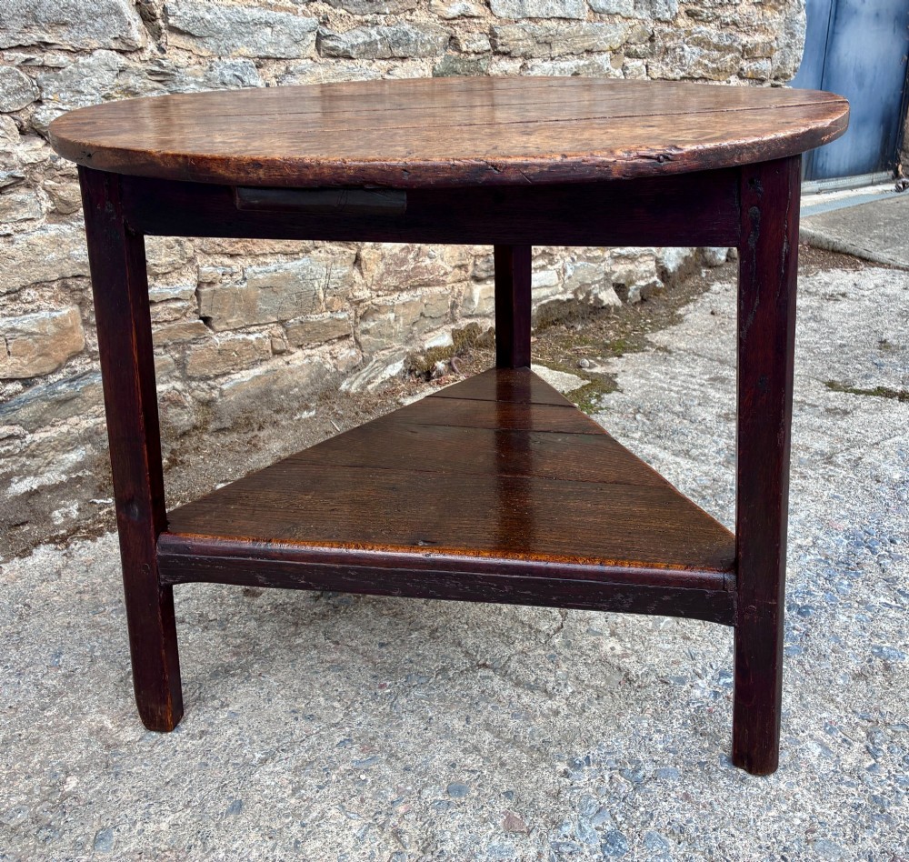 An antique Georgian dark oak cricket table featuring a circular planked top resting on three straight legs with a lower triangular shelf. View VI