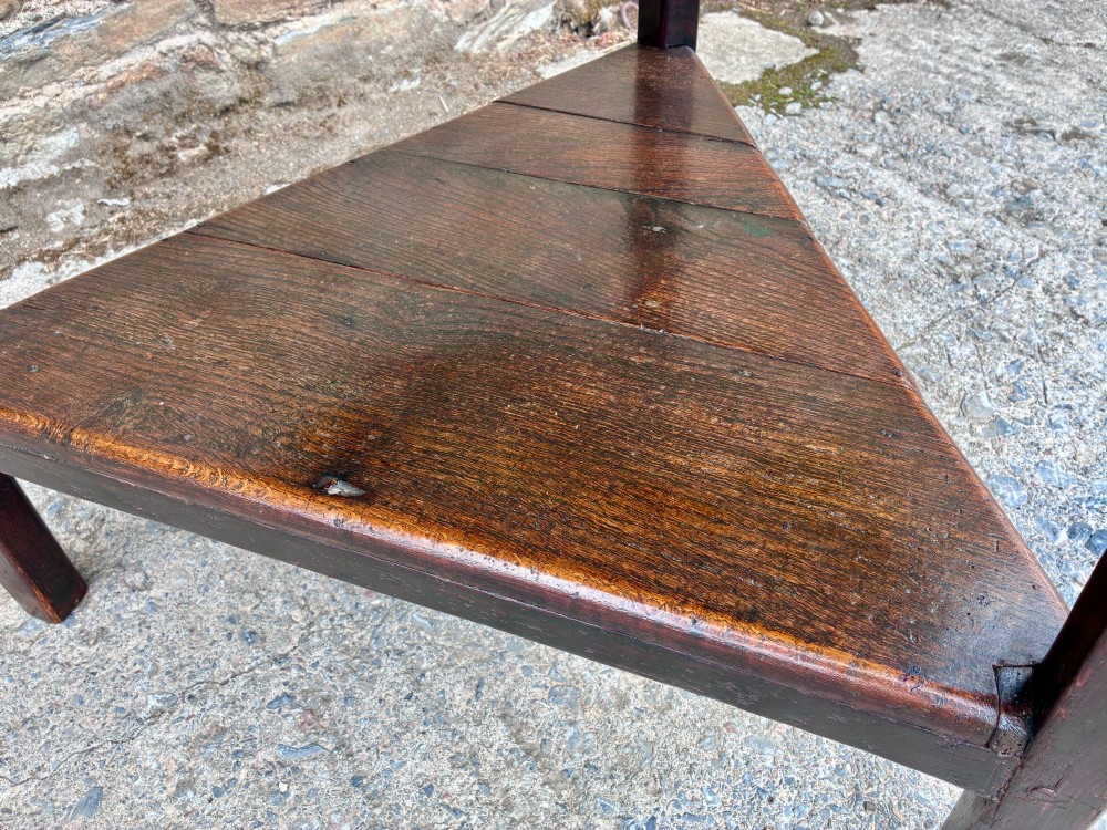 An antique Georgian dark oak cricket table featuring a circular planked top resting on three straight legs with a lower triangular shelf. View VII