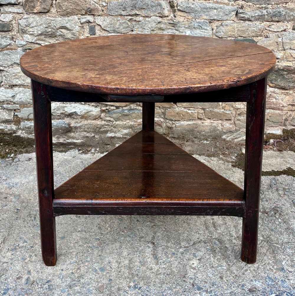 An antique Georgian dark oak cricket table featuring a circular planked top resting on three straight legs with a lower triangular shelf. View VIII
