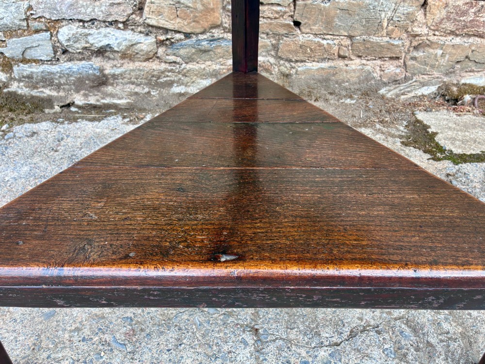 An antique Georgian dark oak cricket table featuring a circular planked top resting on three straight legs with a lower triangular shelf. View IX