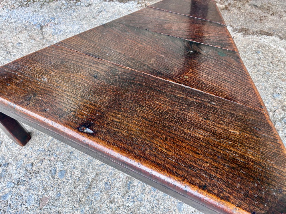 An antique Georgian dark oak cricket table featuring a circular planked top resting on three straight legs with a lower triangular shelf. View X
