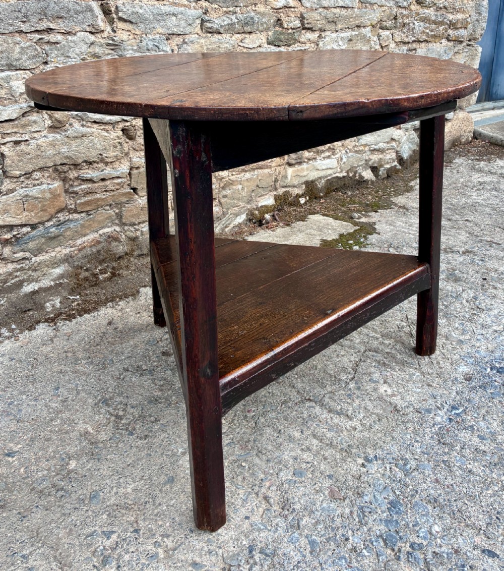An antique Georgian dark oak cricket table featuring a circular planked top resting on three straight legs with a lower triangular shelf. View XI