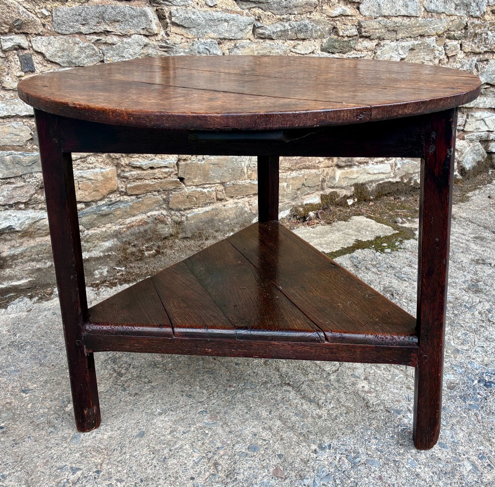 An antique Georgian dark oak cricket table featuring a circular planked top resting on three straight legs with a lower triangular shelf. View XIV