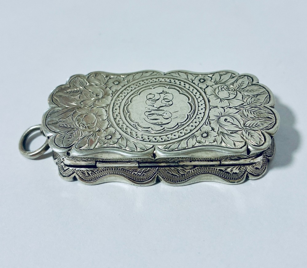 A small rectangular Victorian sterling silver vinaigrette featuring hand-engraved floral motifs, a central monogrammed cartouche, scalloped edges, and a side suspension ring. View III