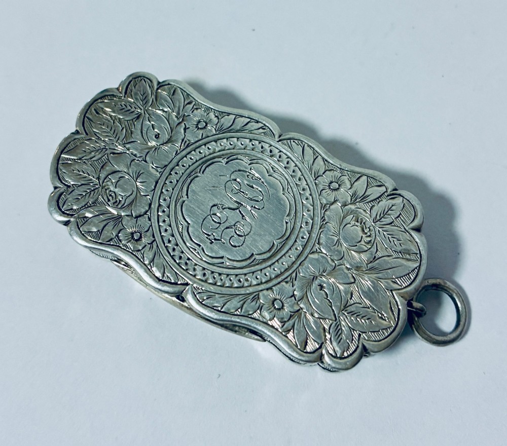 A small rectangular Victorian sterling silver vinaigrette featuring hand-engraved floral motifs, a central monogrammed cartouche, scalloped edges, and a side suspension ring. View IV