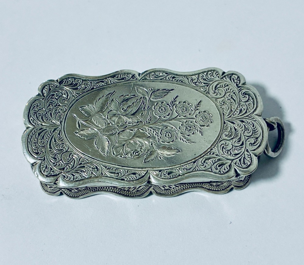 A small rectangular Victorian sterling silver vinaigrette featuring hand-engraved floral motifs, a central monogrammed cartouche, scalloped edges, and a side suspension ring. View V
