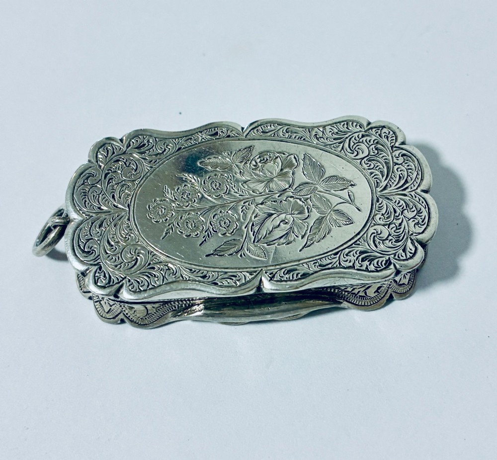 A small rectangular Victorian sterling silver vinaigrette featuring hand-engraved floral motifs, a central monogrammed cartouche, scalloped edges, and a side suspension ring. View VI