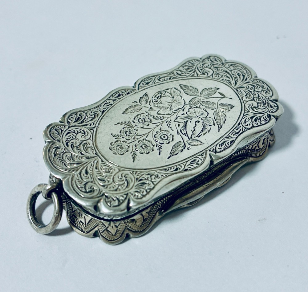 A small rectangular Victorian sterling silver vinaigrette featuring hand-engraved floral motifs, a central monogrammed cartouche, scalloped edges, and a side suspension ring. View VII