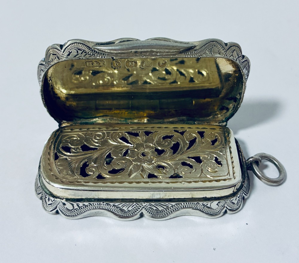 A small rectangular Victorian sterling silver vinaigrette featuring hand-engraved floral motifs, a central monogrammed cartouche, scalloped edges, and a side suspension ring. View VIII