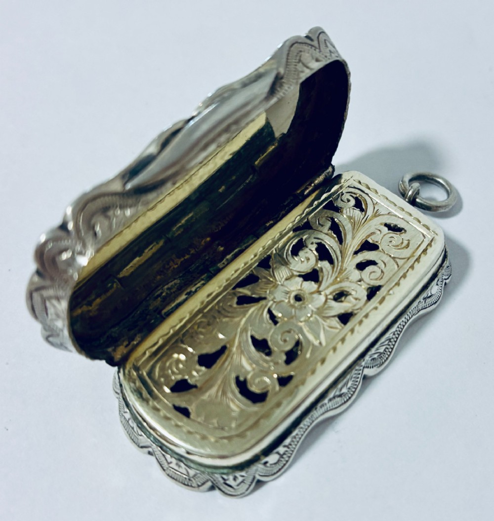 A small rectangular Victorian sterling silver vinaigrette featuring hand-engraved floral motifs, a central monogrammed cartouche, scalloped edges, and a side suspension ring. View X
