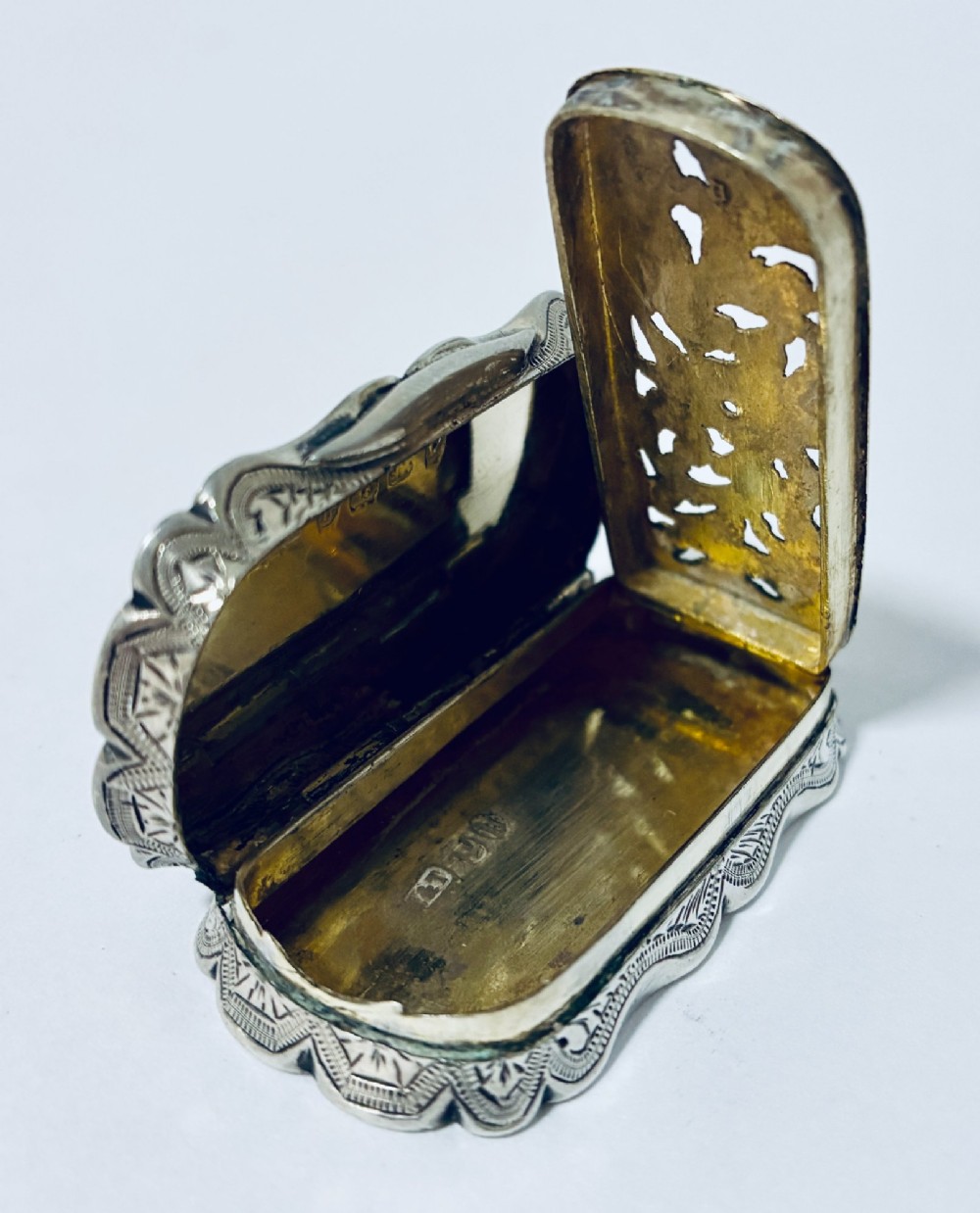 A small rectangular Victorian sterling silver vinaigrette featuring hand-engraved floral motifs, a central monogrammed cartouche, scalloped edges, and a side suspension ring. View XI