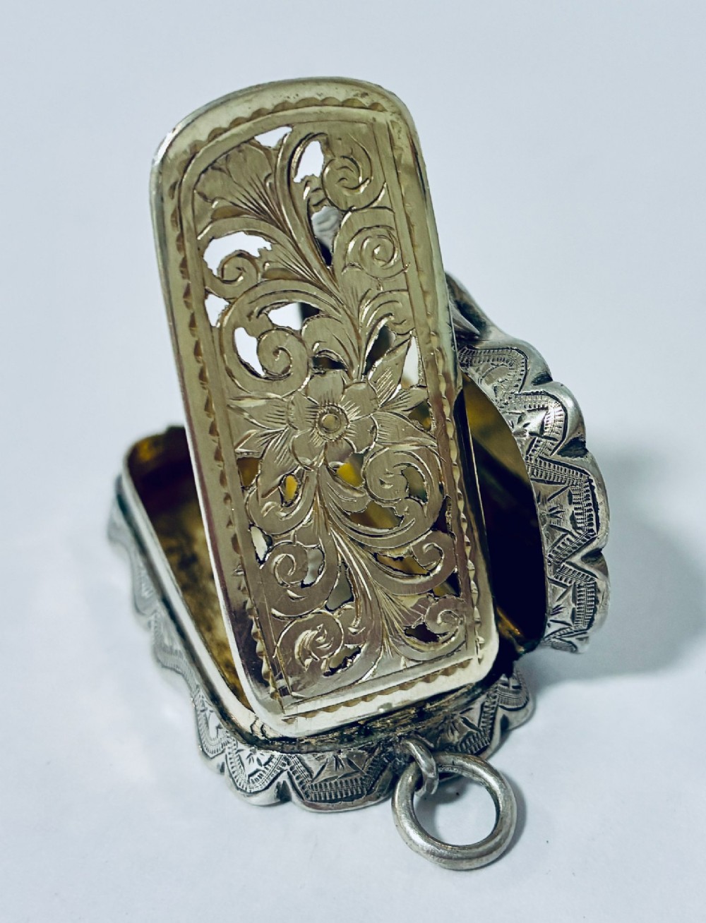 A small rectangular Victorian sterling silver vinaigrette featuring hand-engraved floral motifs, a central monogrammed cartouche, scalloped edges, and a side suspension ring. View XIII