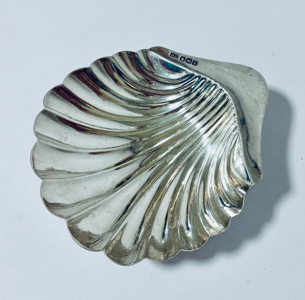 A sterling silver shell-shaped butter dish featuring fluted grooves and visible maker hallmarks on the top rim.