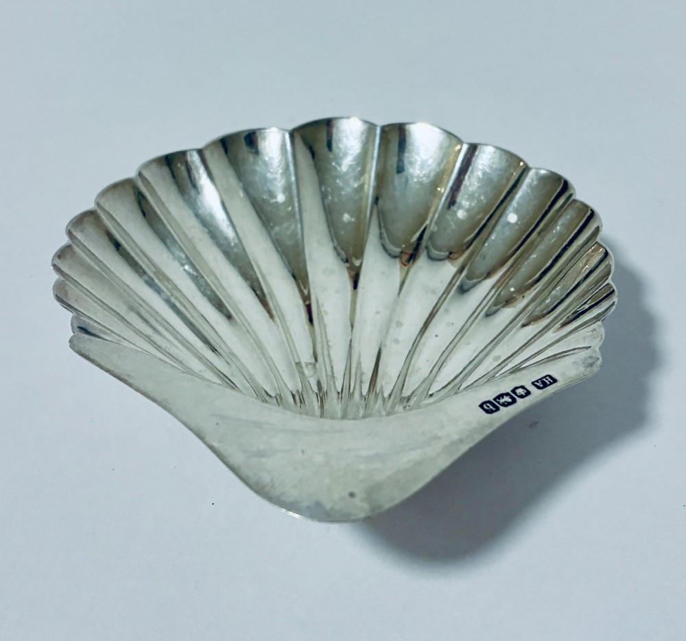 A sterling silver shell-shaped butter dish featuring fluted grooves and visible maker hallmarks on the top rim. View V