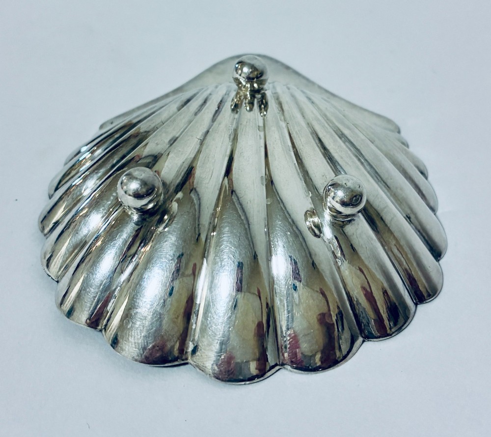 A sterling silver shell-shaped butter dish featuring fluted grooves and visible maker hallmarks on the top rim. View VI