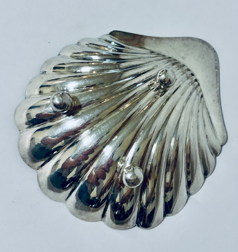 A sterling silver shell-shaped butter dish featuring fluted grooves and visible maker hallmarks on the top rim. View VII