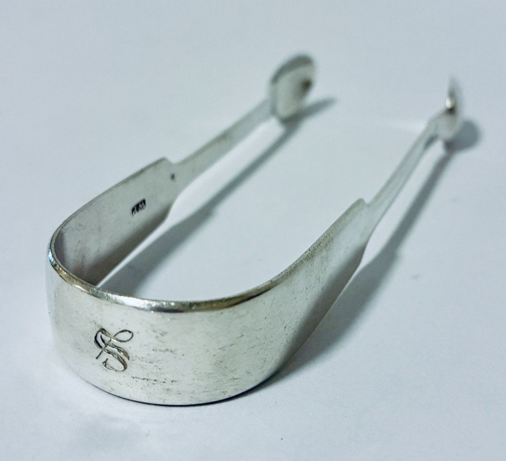 A pair of plain polished sterling silver sugar tongs with spoon-shaped grips and assay hallmarks stamped along the inner curve. View II