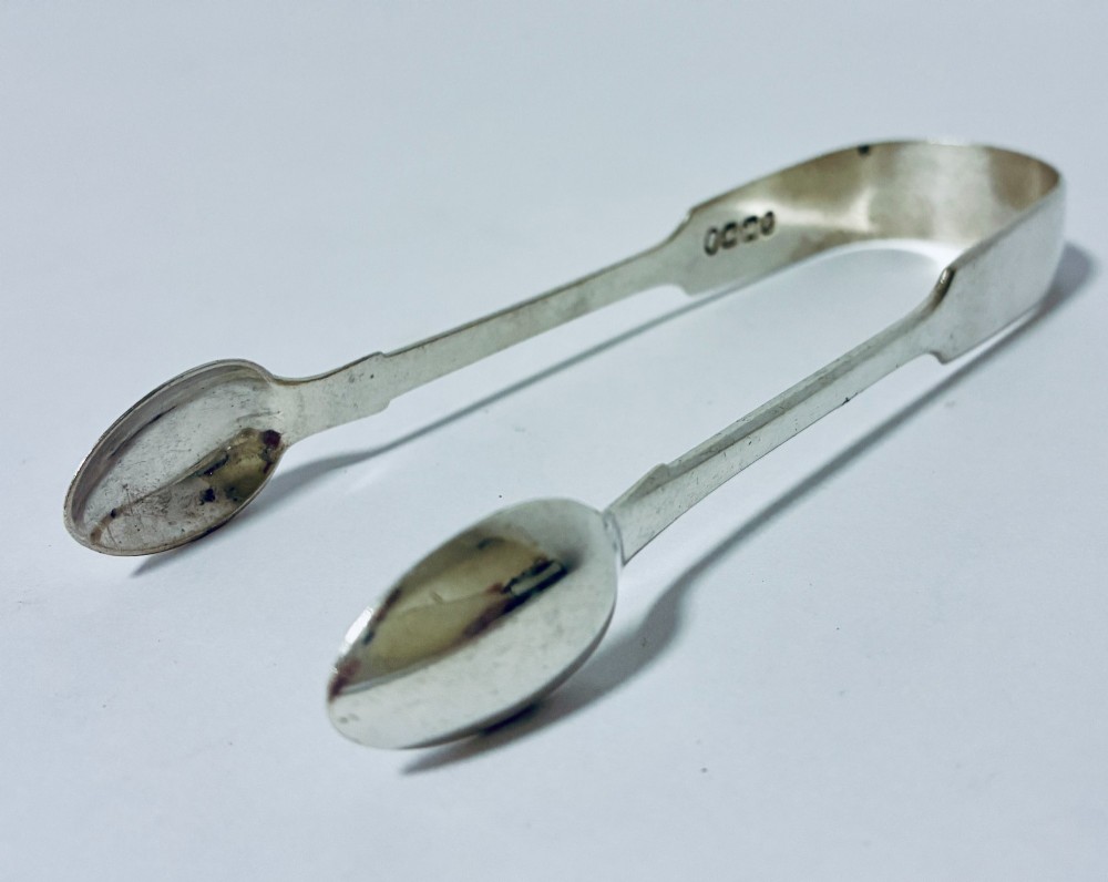 A pair of plain polished sterling silver sugar tongs with spoon-shaped grips and assay hallmarks stamped along the inner curve. View VI