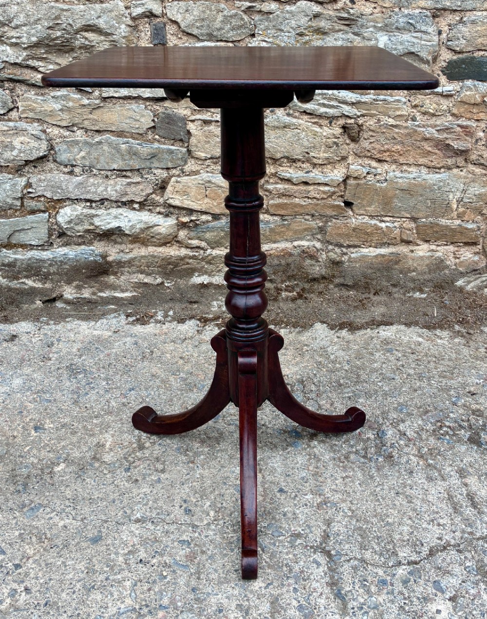 A Regency era dark mahogany tilt-top wine table featuring a rectangular surface, turned central pedestal stem, and a splayed tripod base. View II