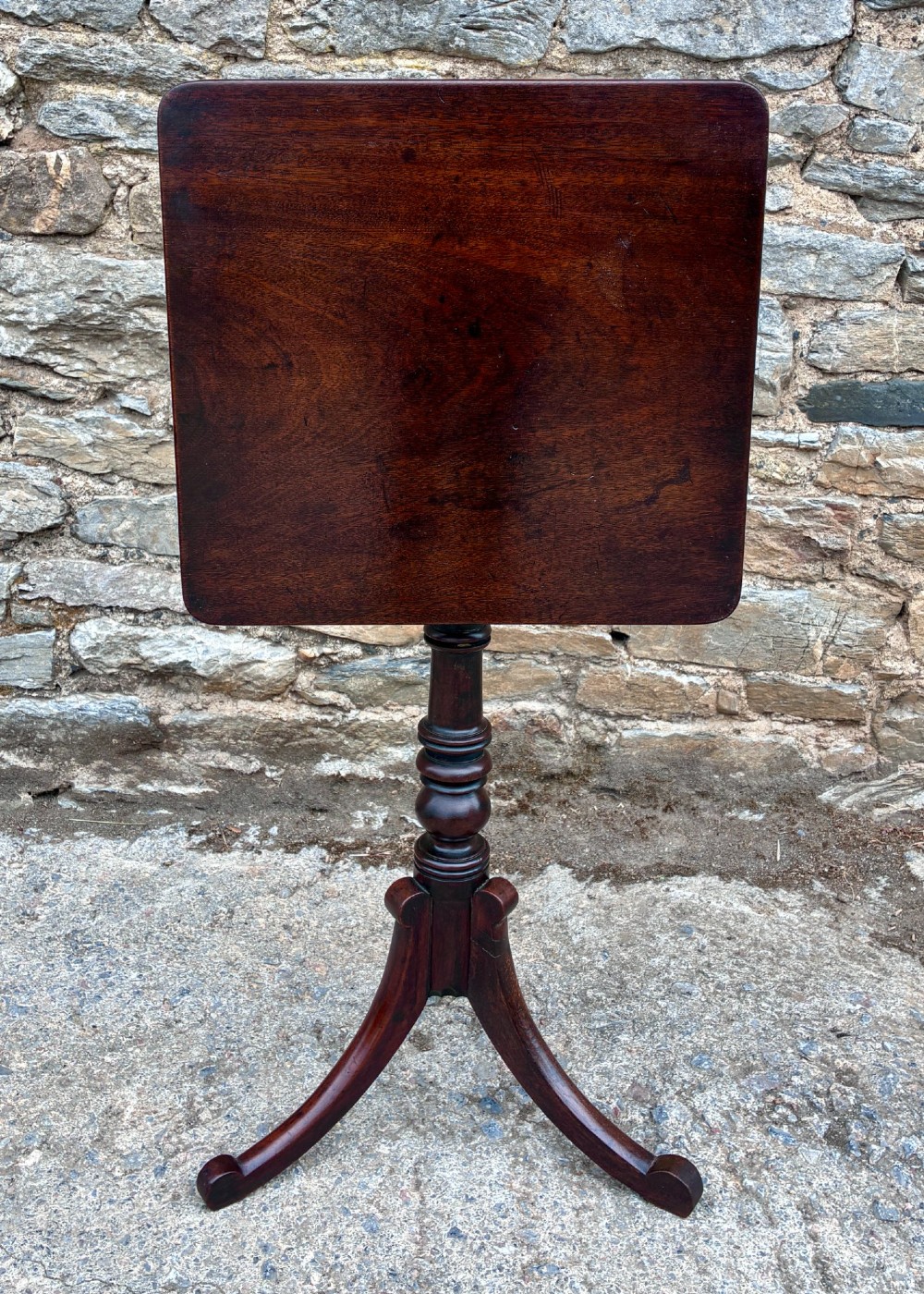 A Regency era dark mahogany tilt-top wine table featuring a rectangular surface, turned central pedestal stem, and a splayed tripod base. View X