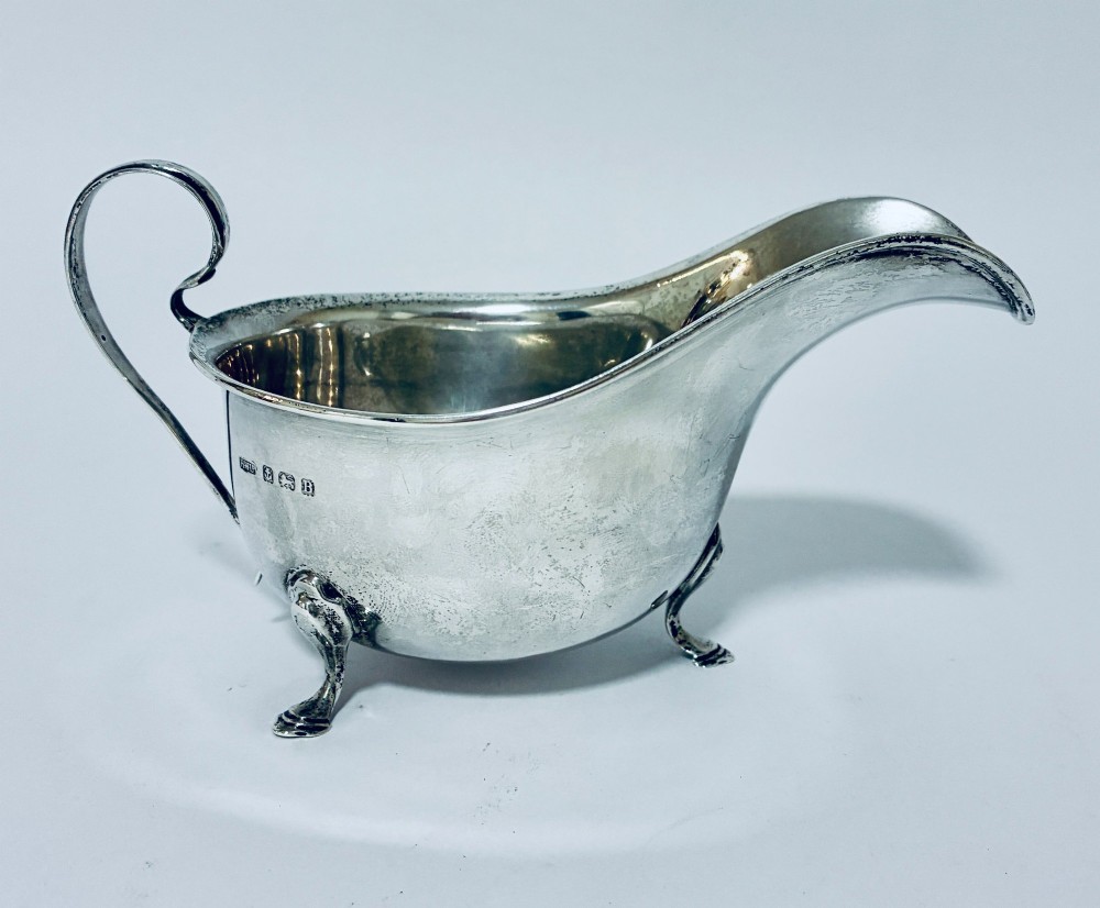 An antique silver sauce boat featuring a scrolled flying handle, flared pouring spout, and three cast pad feet. View III