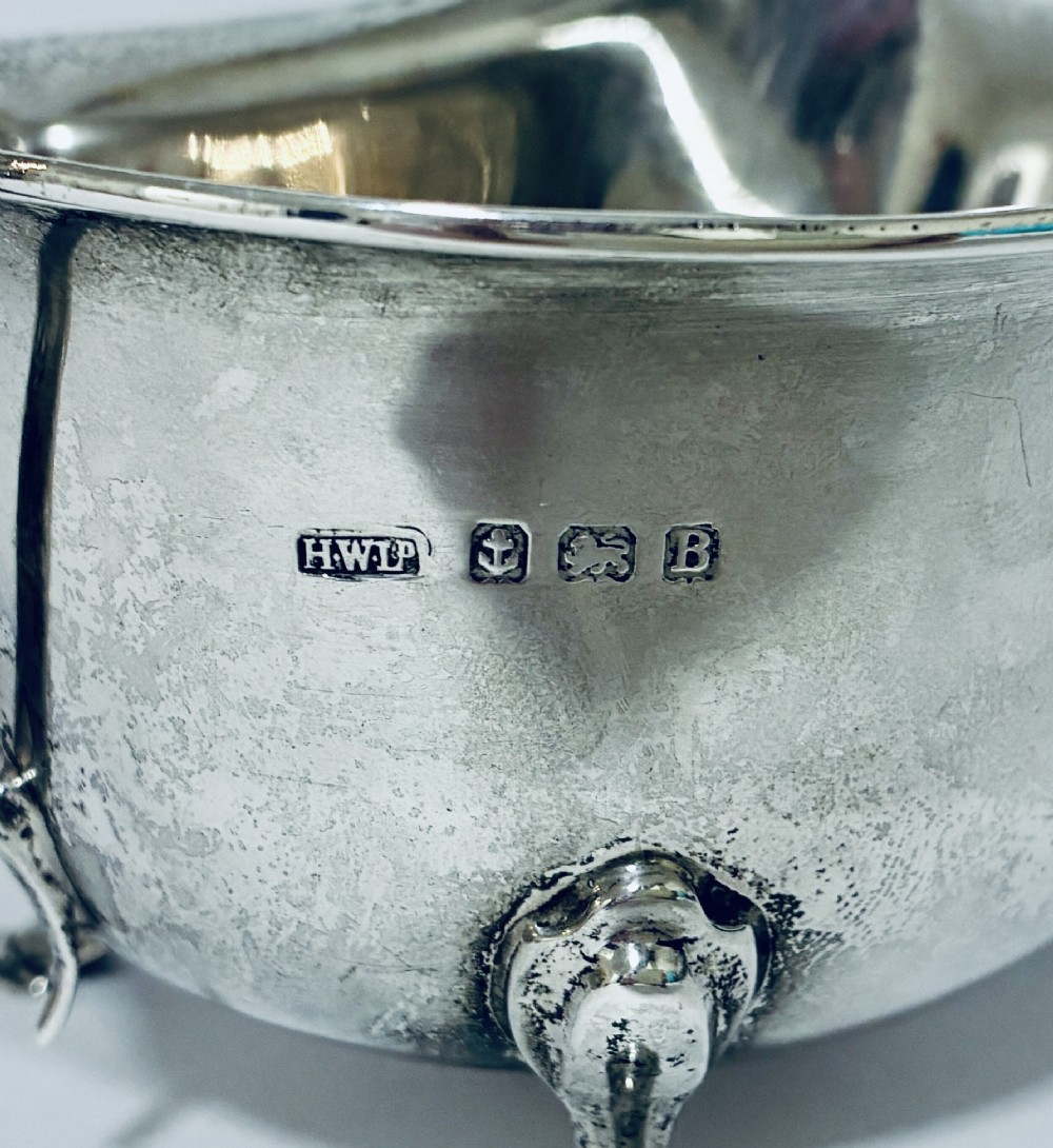 An antique silver sauce boat featuring a scrolled flying handle, flared pouring spout, and three cast pad feet. View IV