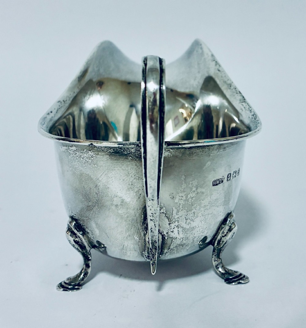 An antique silver sauce boat featuring a scrolled flying handle, flared pouring spout, and three cast pad feet. View V