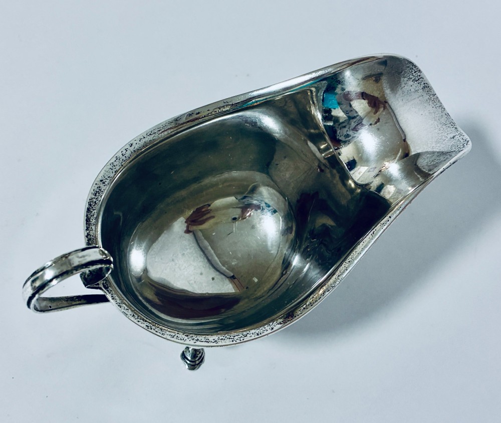 An antique silver sauce boat featuring a scrolled flying handle, flared pouring spout, and three cast pad feet. View VI