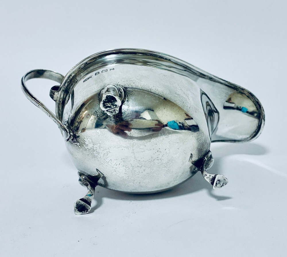 An antique silver sauce boat featuring a scrolled flying handle, flared pouring spout, and three cast pad feet. View VII