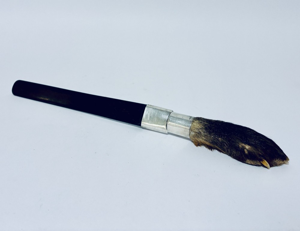 An antique page turner featuring a dark ebony blade connected via a silver collar to an otter paw handle.