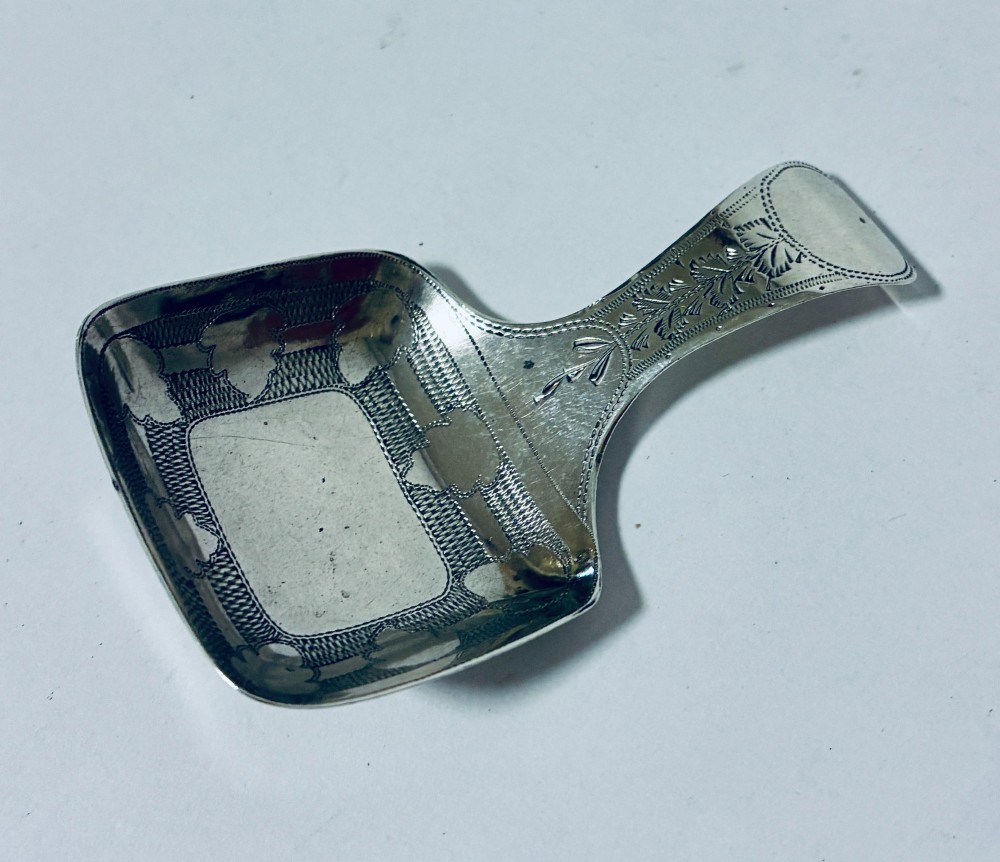 A Georgian sterling silver caddy spoon with a rectangular shovel-form bowl and bright-cut engraved geometric patterns on the handle.