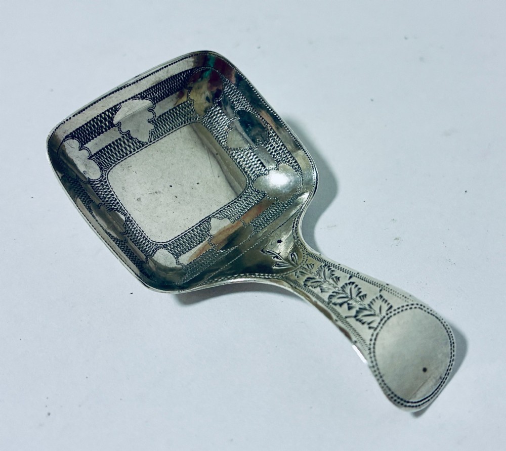 A Georgian sterling silver caddy spoon with a rectangular shovel-form bowl and bright-cut engraved geometric patterns on the handle. View IV