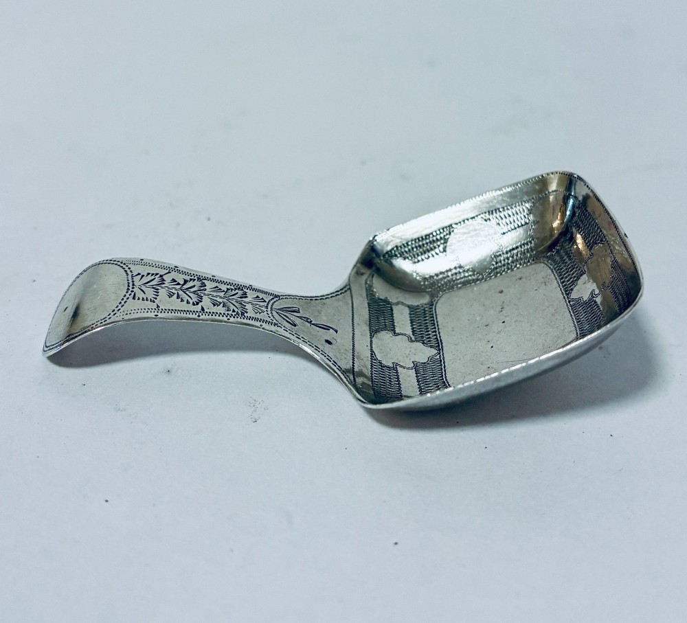 A Georgian sterling silver caddy spoon with a rectangular shovel-form bowl and bright-cut engraved geometric patterns on the handle. View V