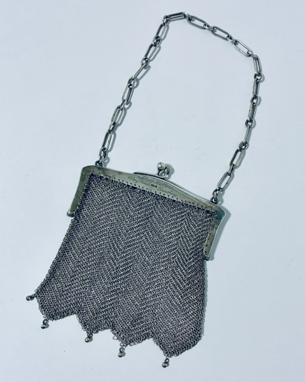 An Art Deco silver mesh purse featuring an engraved kiss-lock frame, a paperclip link chain handle, and a scalloped hem with drop-bead detailing.
