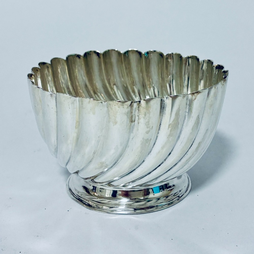 An antique silver pedestal bowl featuring spiralled fluted sides and a scalloped rim resting on a round moulded base.