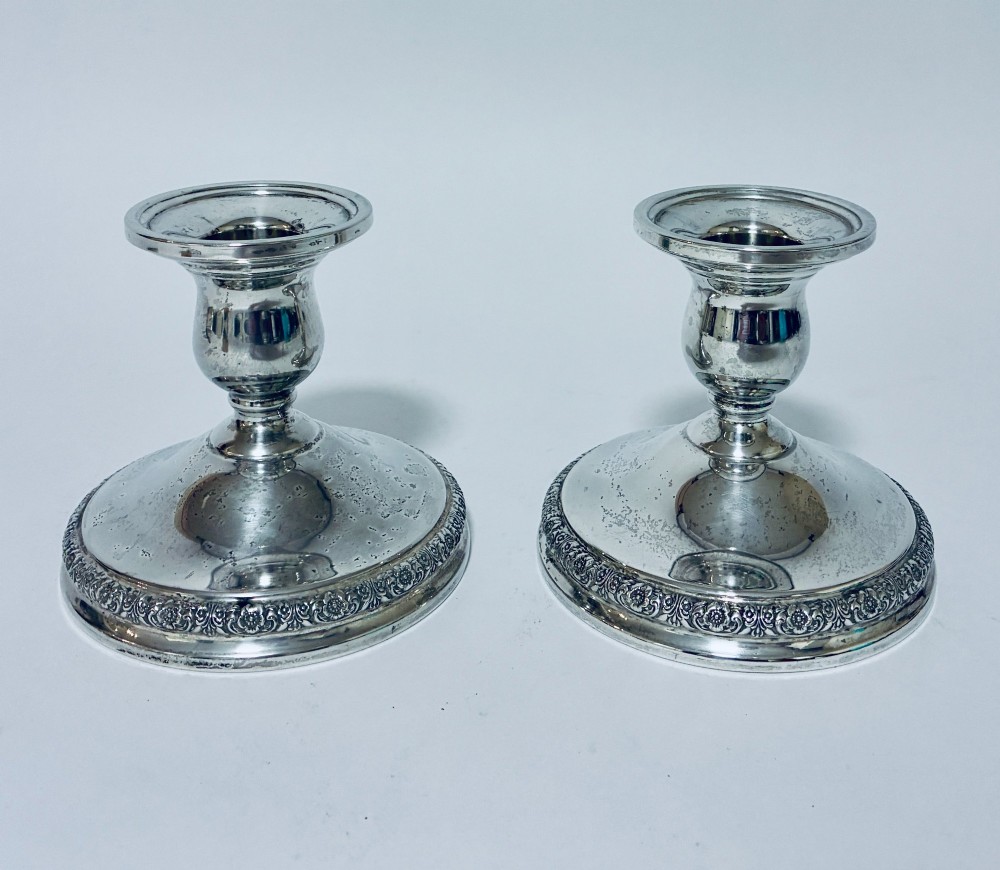 A pair of short sterling silver desk candlesticks featuring round bases with chased floral borders and baluster stems.