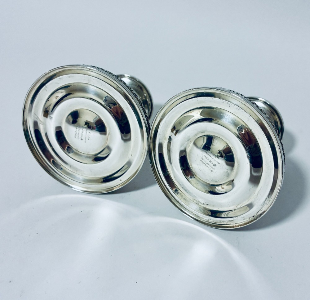 A pair of short sterling silver desk candlesticks featuring round bases with chased floral borders and baluster stems. View V