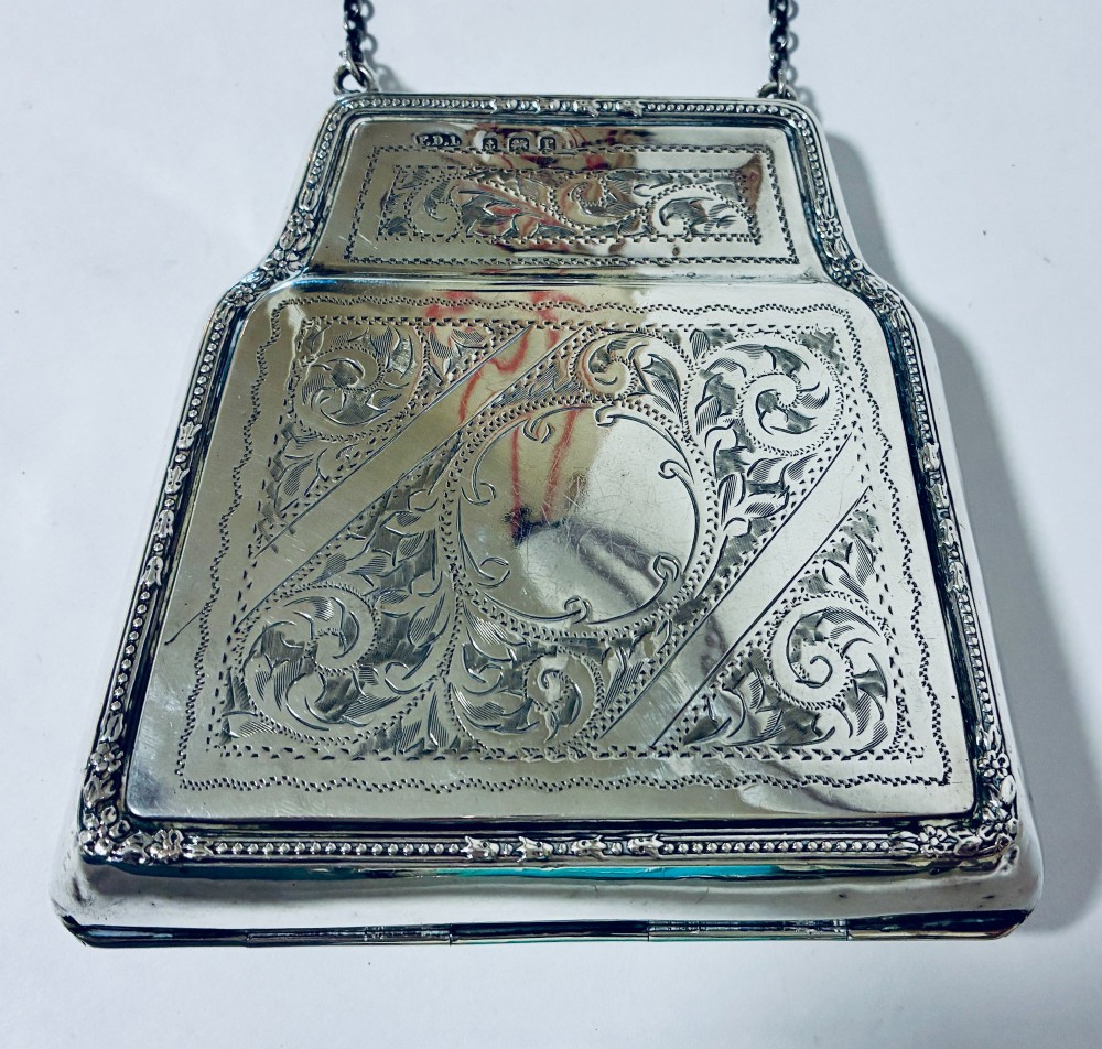 An antique sterling silver evening purse featuring engraved floral scrollwork, visible hallmarks along the upper frame, and a chain handle with a finger ring. View III